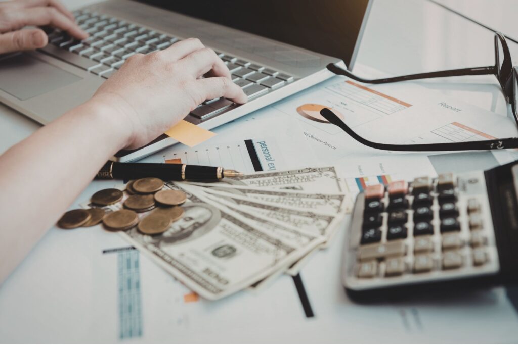 An entrepreneur managing business finances with a laptop, calculator, and cash to organize personal vs business expenses.
