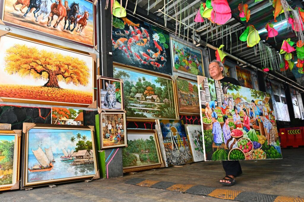 Man walking past a wall hung with colorful paintings.