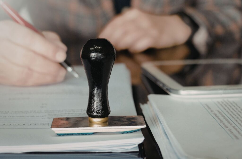Close up shot of a stamp on top of official forms being filled in by an individual.