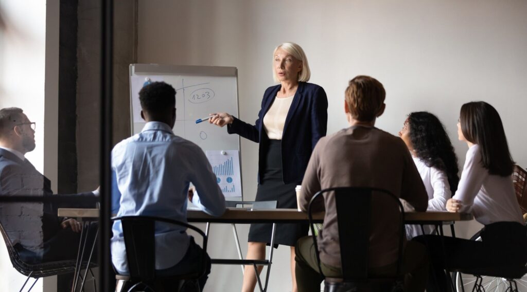 A woman presenting to a few of her colleagues in an office meeting room.