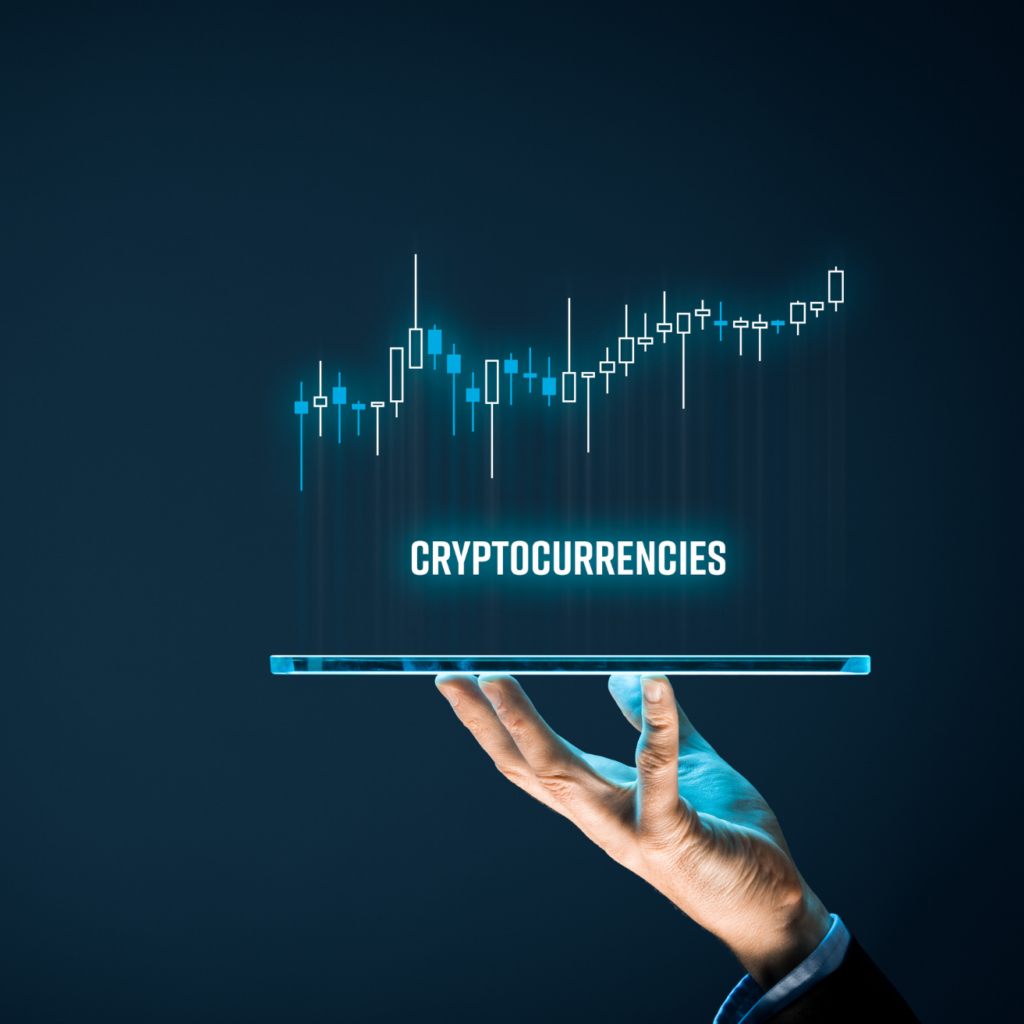 A close-up shot features a hand holding up a glowing, transparent tablet screen against a dark blue, abstract background. The screen displays the word "CRYPTOCURRENCIES" in bright, glowing white text, above which is a neon blue candlestick chart showing an overall upward trend..