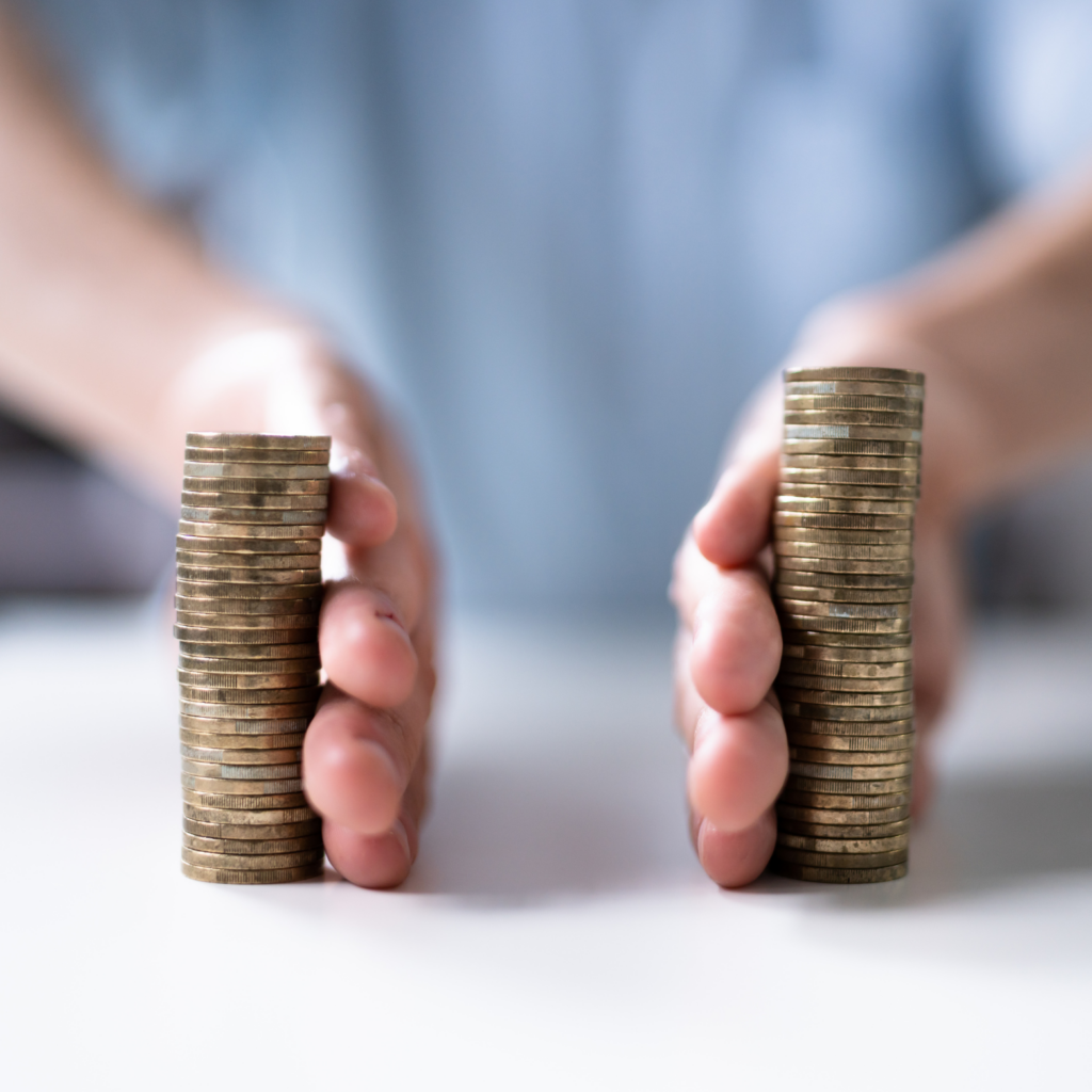 A close-up shot of two stacks of gold coins, with a pair of hands on the left and right side, suggesting the segregation or division of funds. The background is blurred, showing a person in a light blue or white shirt. The image illustrates the concepts of a segregated account or segregated funds.